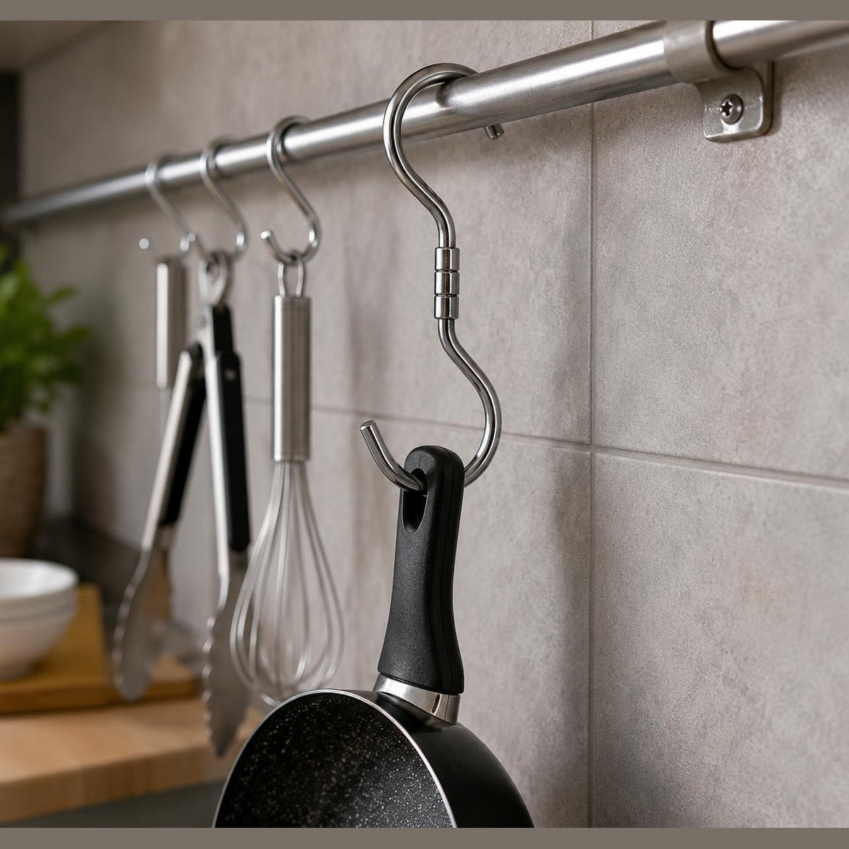 Gancio girevole in acciaio da 260x10 mm utilizzato in cucina per appendere una padella a una barra metallica portautensili.