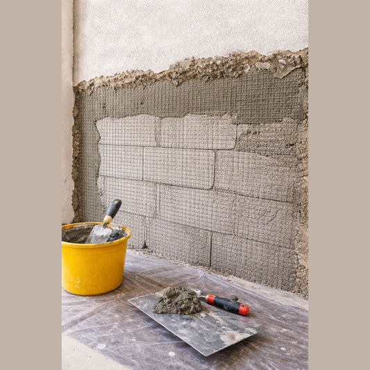 Rete per intonaco e massetto in metallo applicata su una parete con mattoni a vista e attrezzi da lavoro in primo piano.